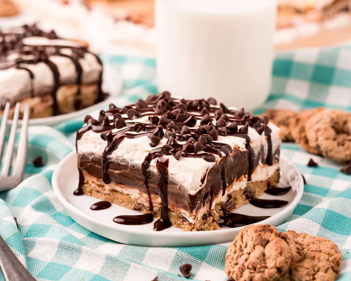 A piece of layered chocolate hip cookie lasagna on a small plate, topped with mini chocolate chips, and drizzled with chocolate syrup.