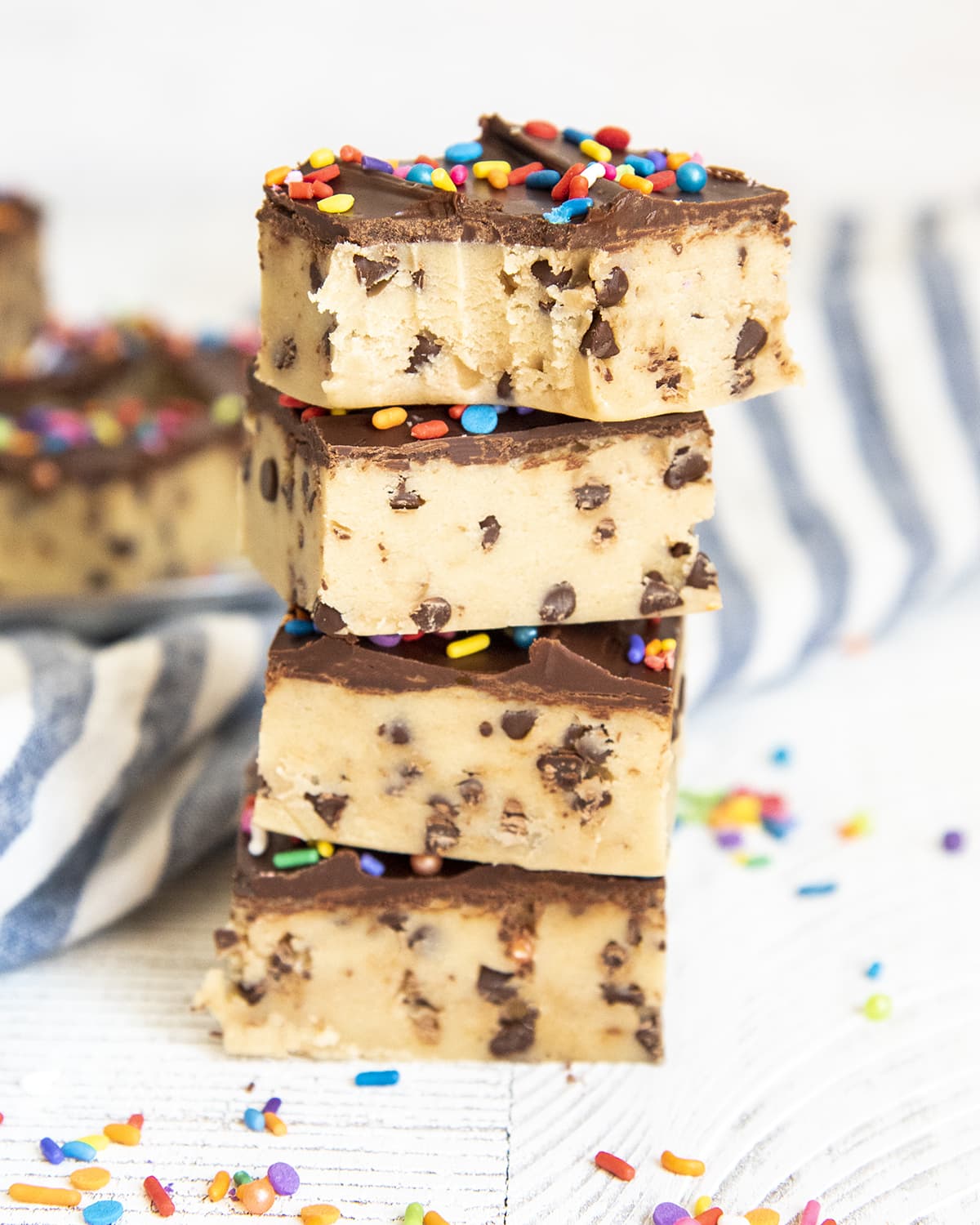 A stack of chocolate chip cookie dough bars, topped with a thin layer of chocolate. The top is bitten into.