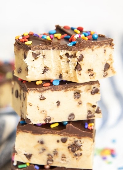 A stack of chocolate chip cookie dough bars, topped with a thin layer of chocolate. The top is bitten into.