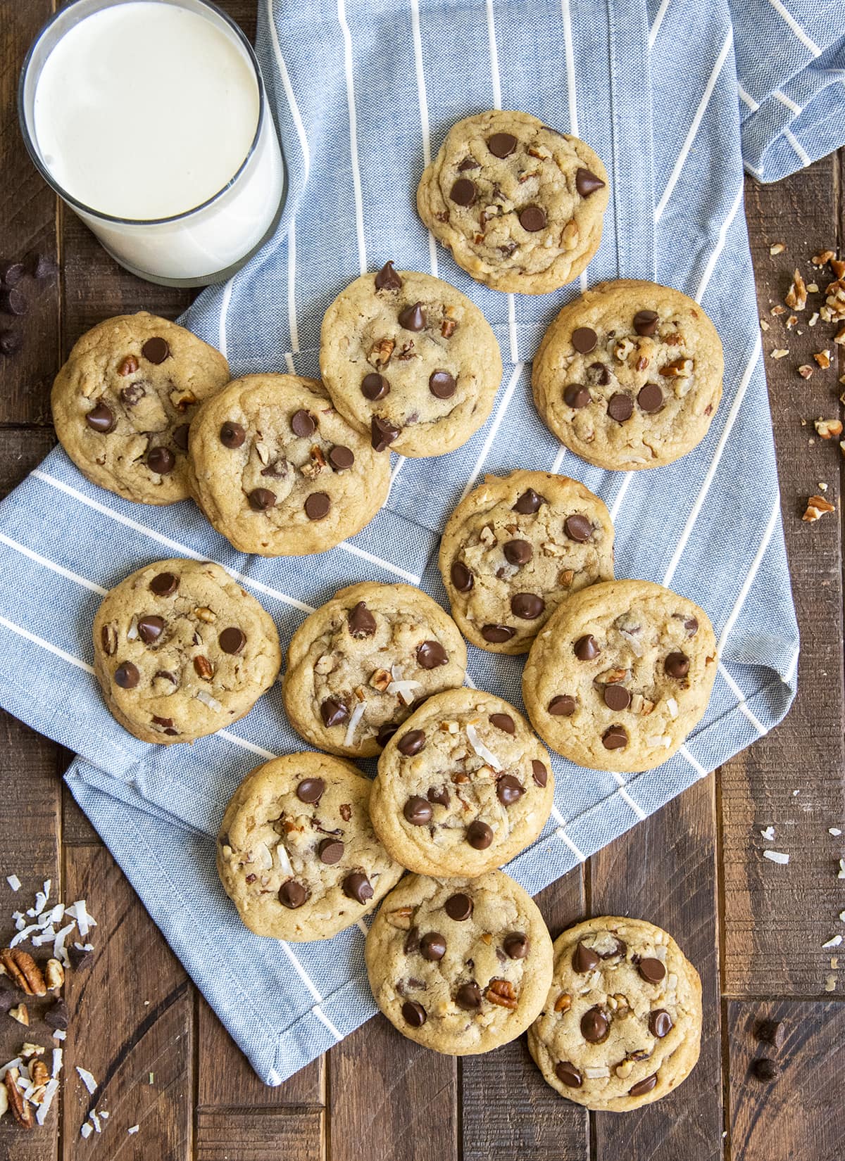 Coconut pecan chocolate chip cookies arranged randomly scattered over the top of a blue striped cloth.