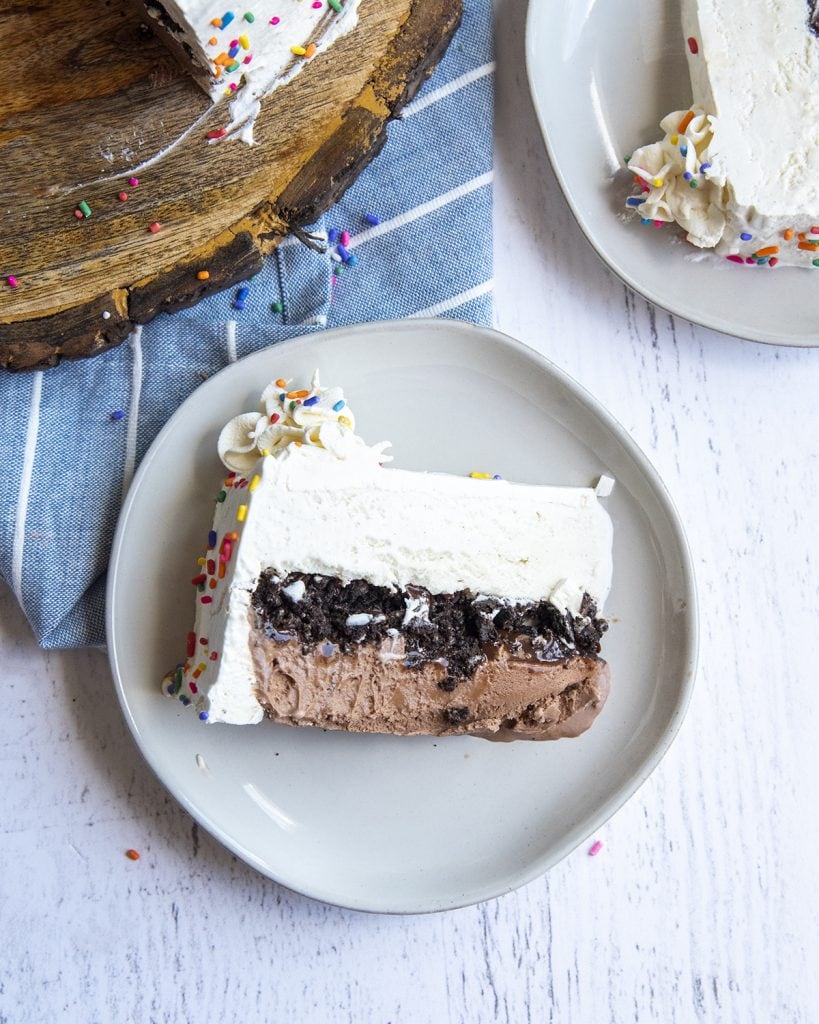 A piece of ice cream cake on a plate, with a layer of chocolate ice cream, cookie crumbs, and vanilla ice cream.
