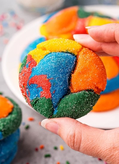 A hand holding a rainbow swirled cookie, with red, yellow, orange, blue and green colors.