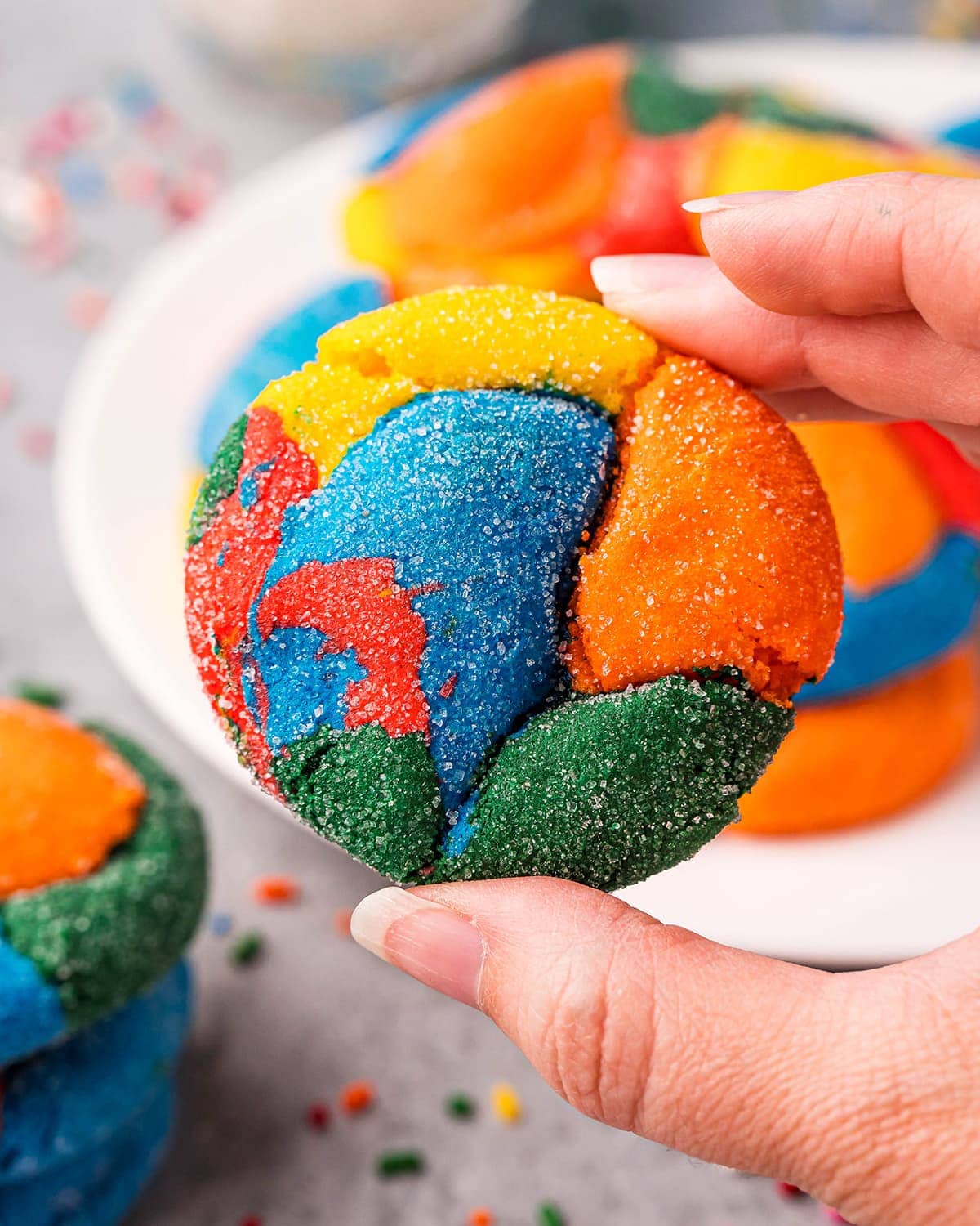 A hand holding a rainbow swirled cookie, with red, yellow, orange, blue and green colors.