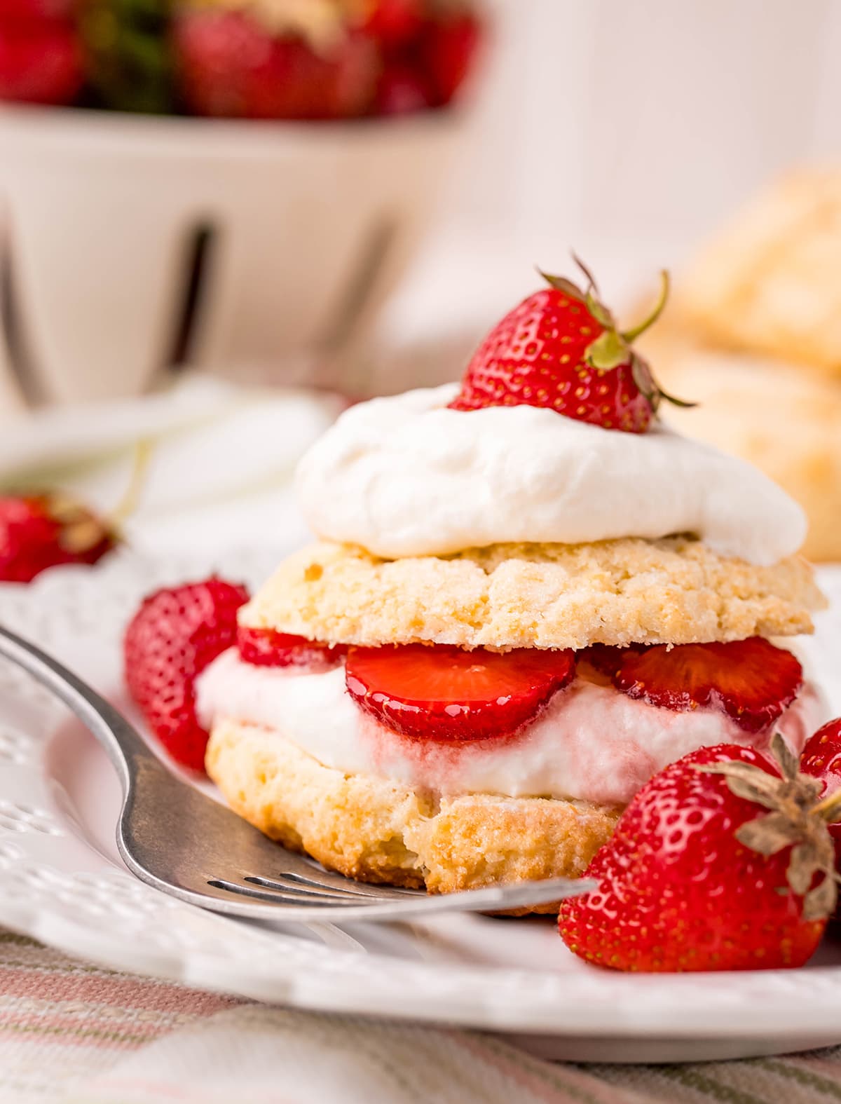 A biscuit strawberry shortcake layered with whipped cream and sliced strawberries on a white plate. 