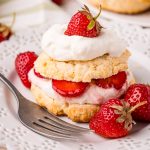 Strawberry shortcakes on a plate with layers of whipped cream and strawberries.