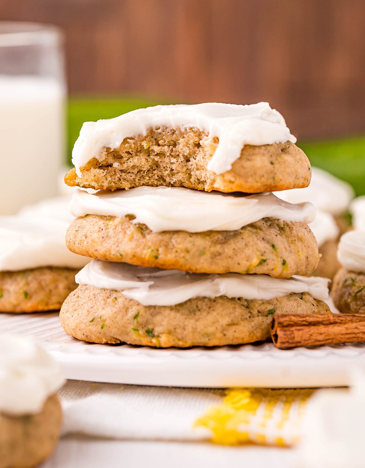 A stack of three zucchini cookies, and the top cookie has a bite out of it. The cookies are topped with cream cheese frosting.