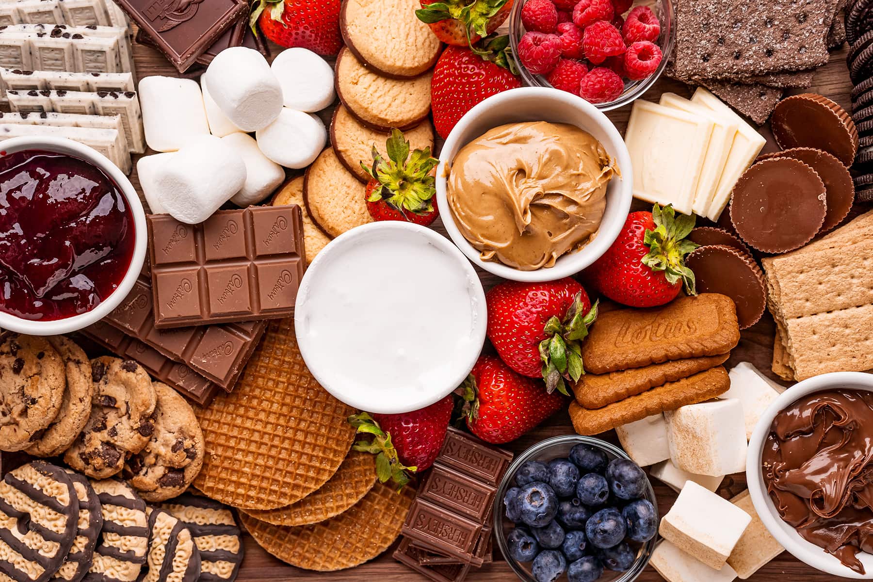 A s'mores board full of cookie choices, fresh berries, chocolate and dips to make a variety of s'mores.