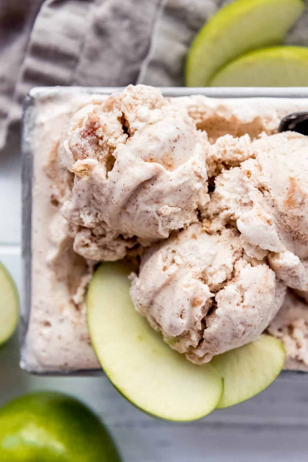 An overhead photo of scoops of cinnamon ice cream in a metal container with slices of green apples next to it. 