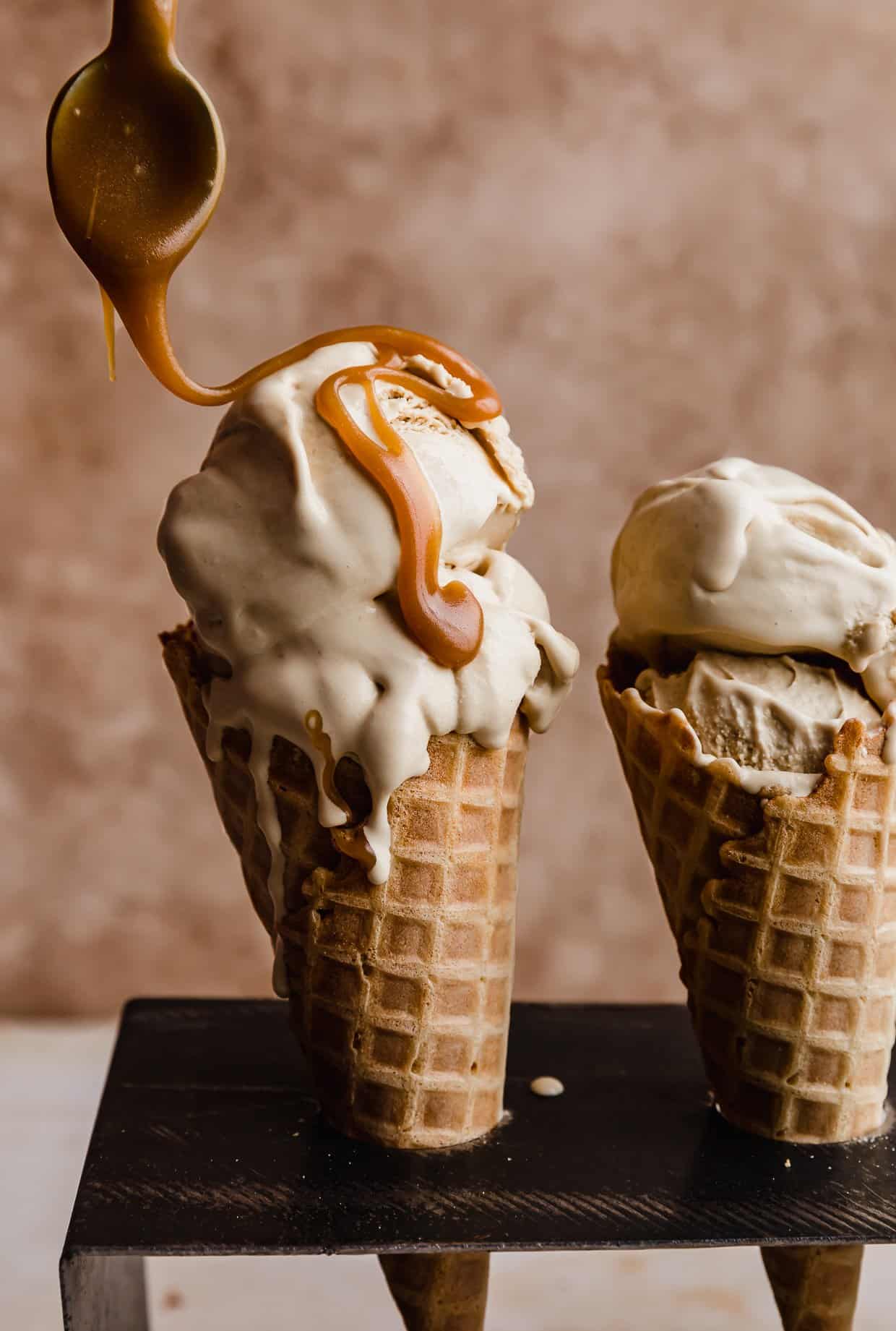 A butterscotch ice cream cone with butterscotch drizzled over the top with a spoon.