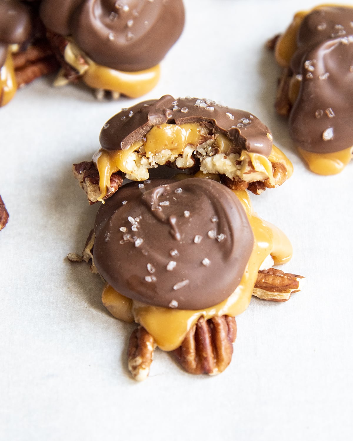 Two chocolate turtle candies piled on top of one another, one has a bite out of it.