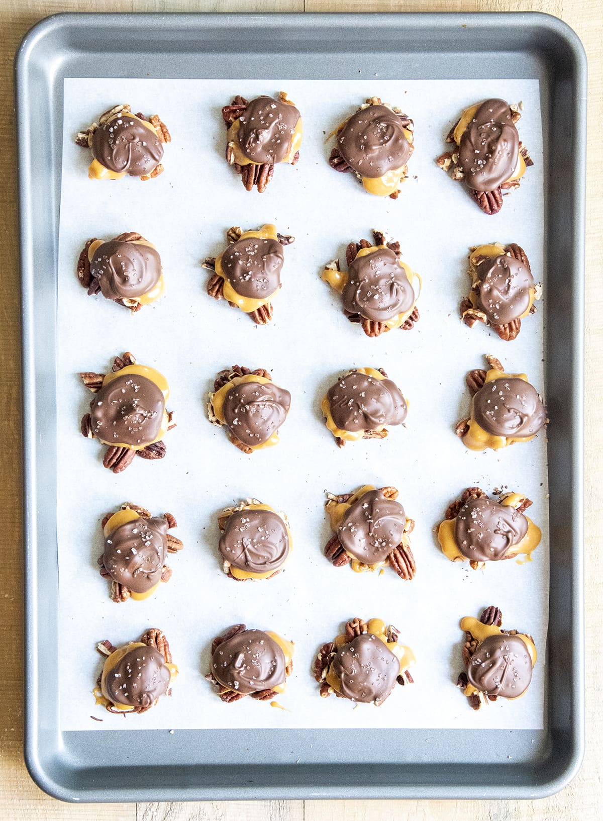 A cookie sheet topped with rows of homemade chocolate turtle candies