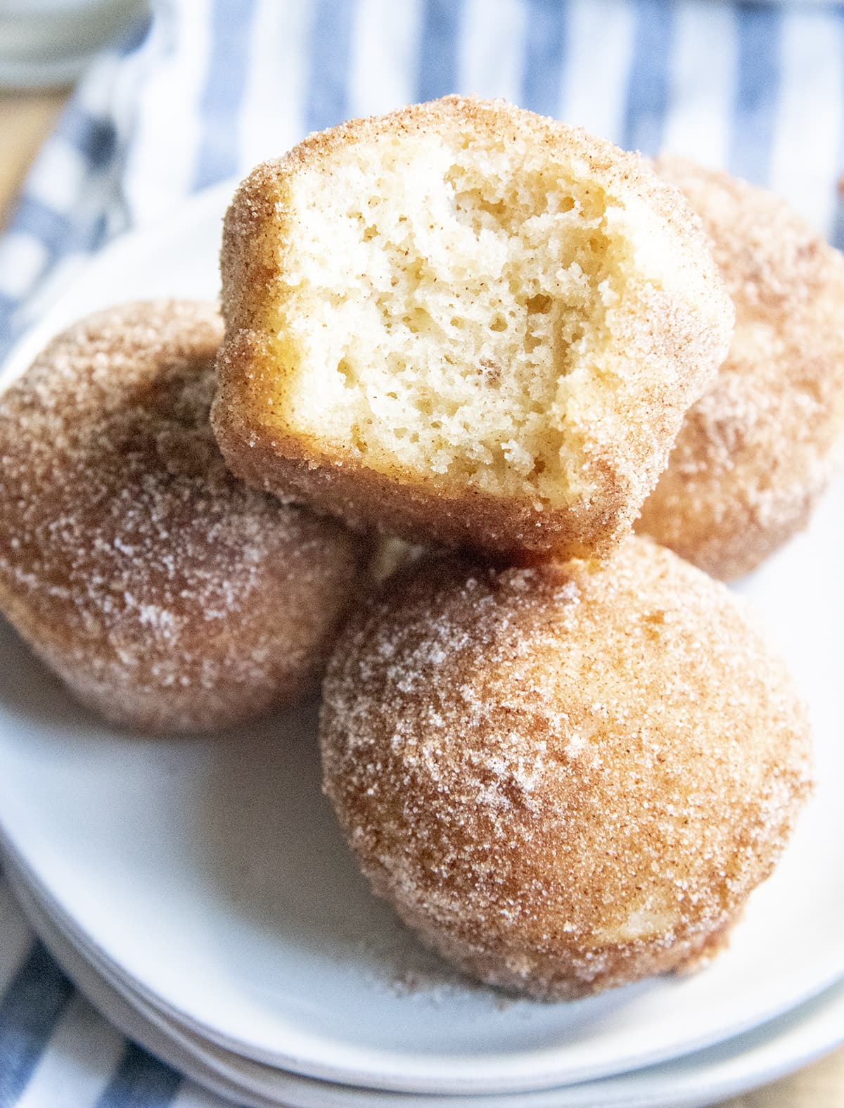 A pile of muffins coated in cinnamon sugar, the top muffin has a bite out of it showing the middle of the muffin.
