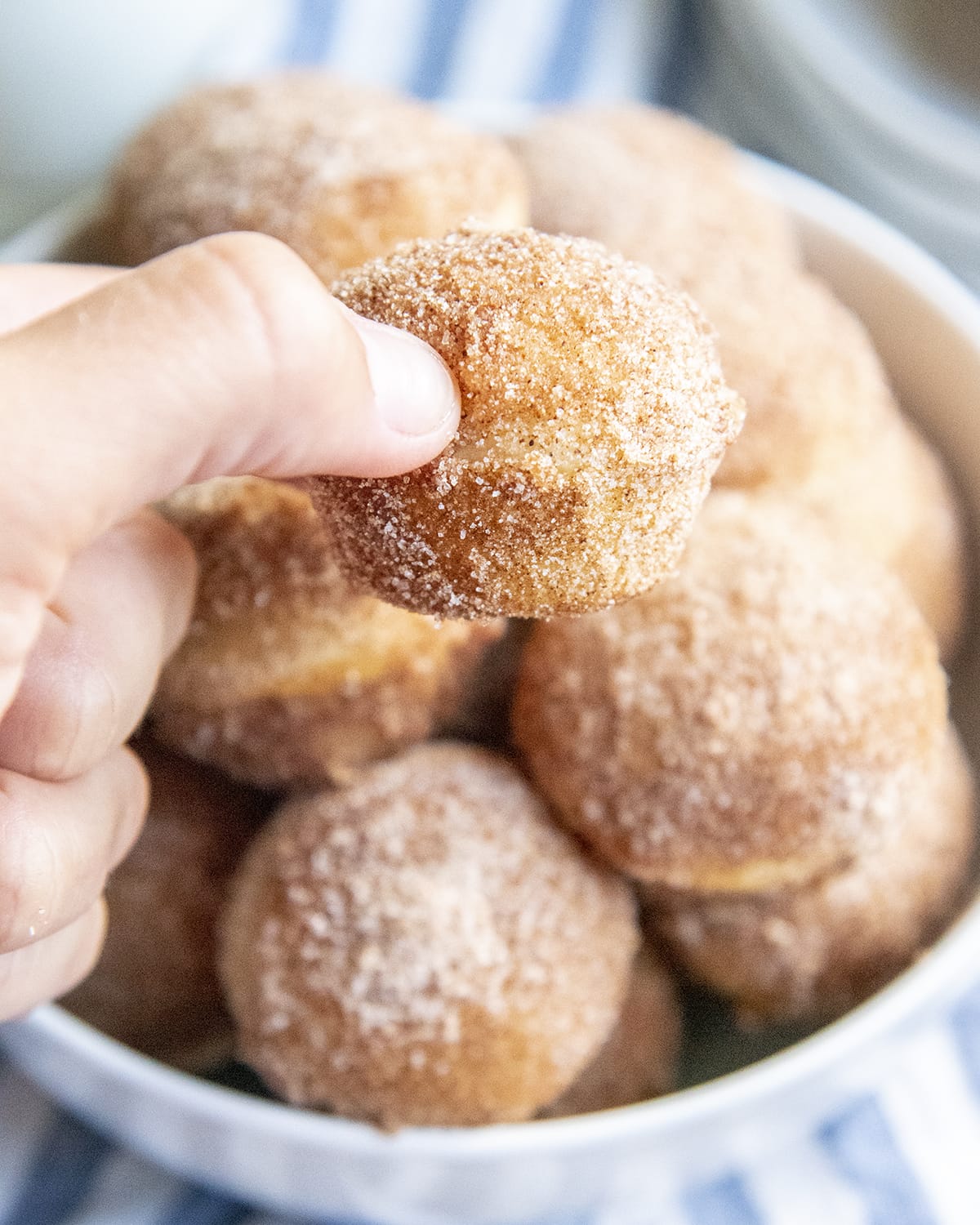 A hand holding a mini cinnamon sugar muffin above a bowl of them.