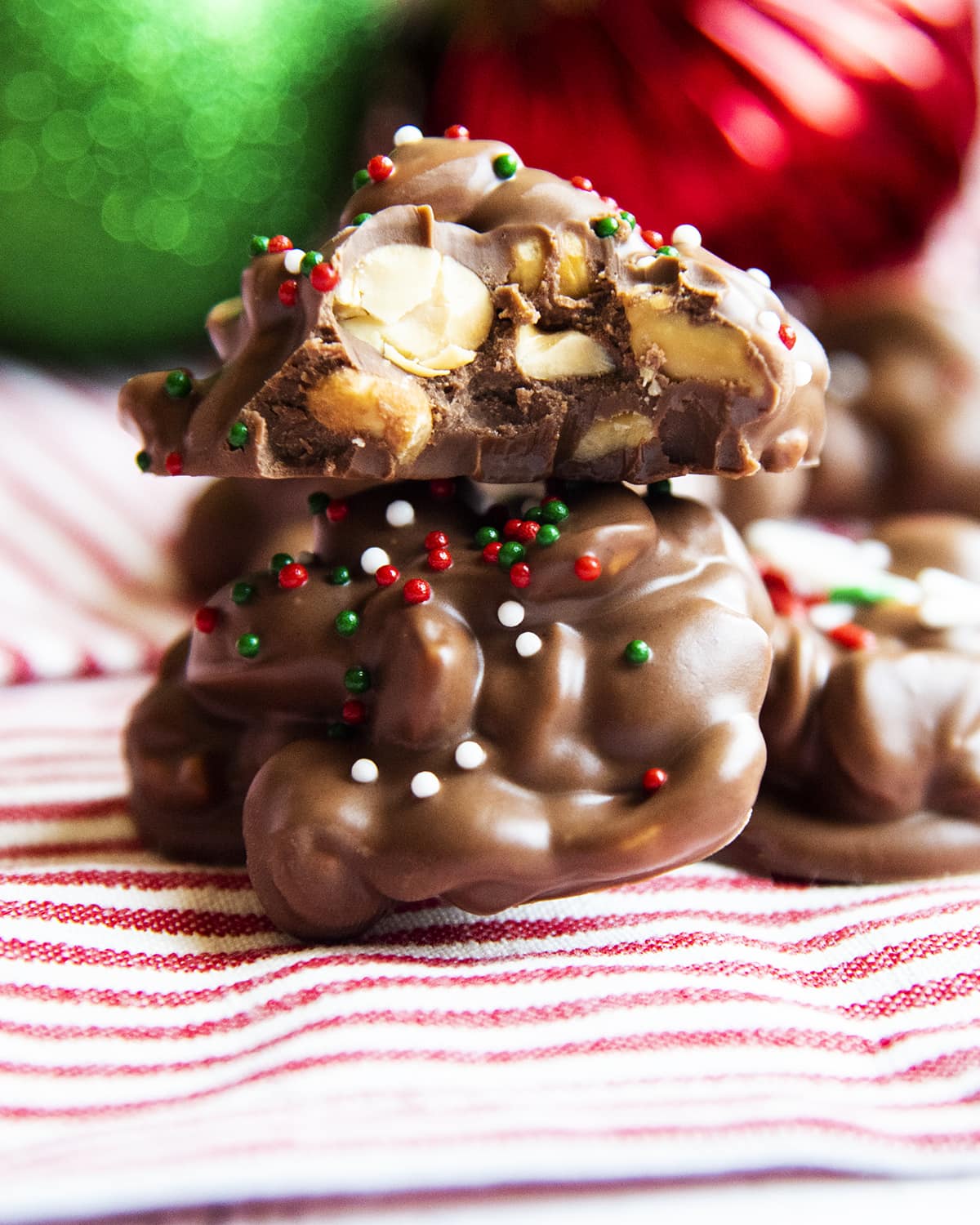 Two peanut clusters stacked and the top is bit in half showing the peanuts covered in chocolate.