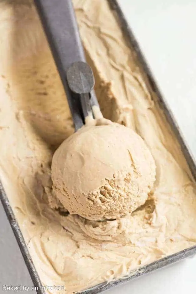 A container of coffee ice cream with a big scoop of ice cream in an ice cream scoop on top.