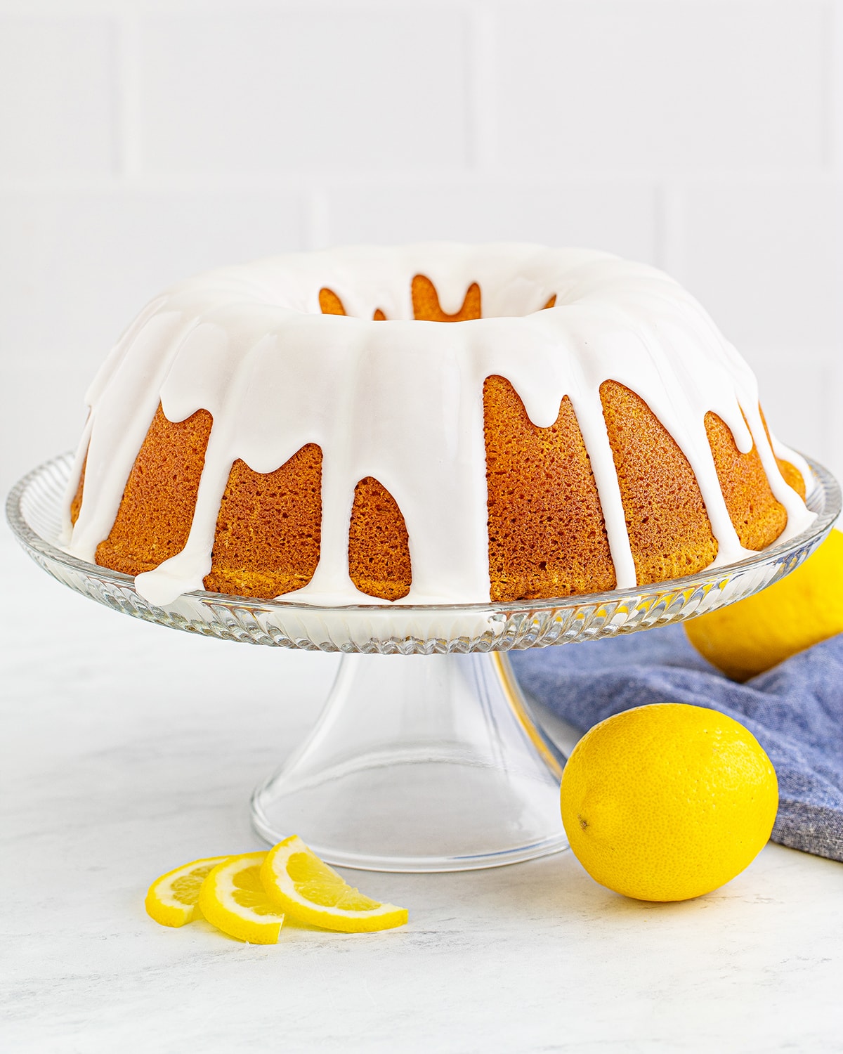 A bundt cake on a glass cake stand covered in a white glaze. 