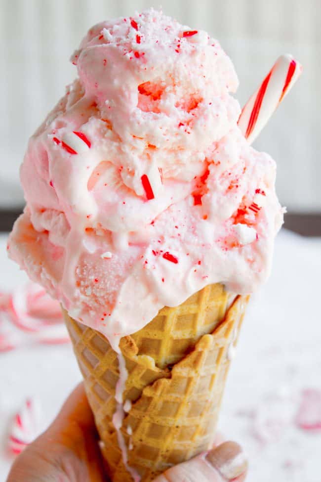A hand holding an ice cream cone topped with pink peppermint ice cream.