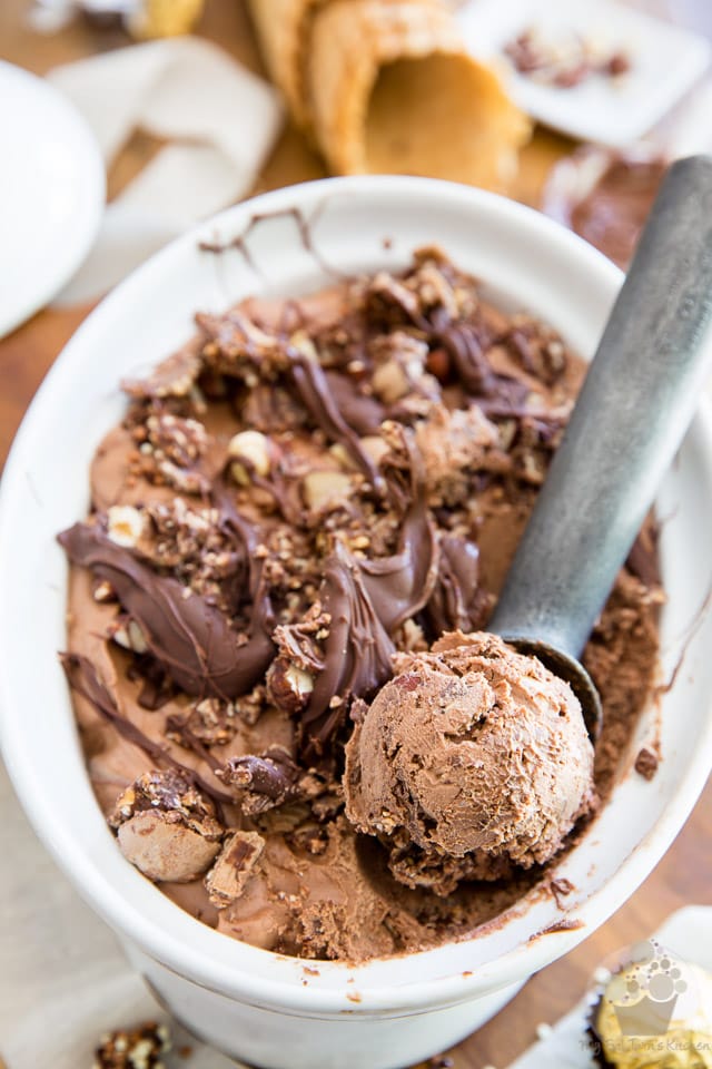 A white container full of Nutella ice cream topped with thick Nutella swirls and chopped hazelnuts. 