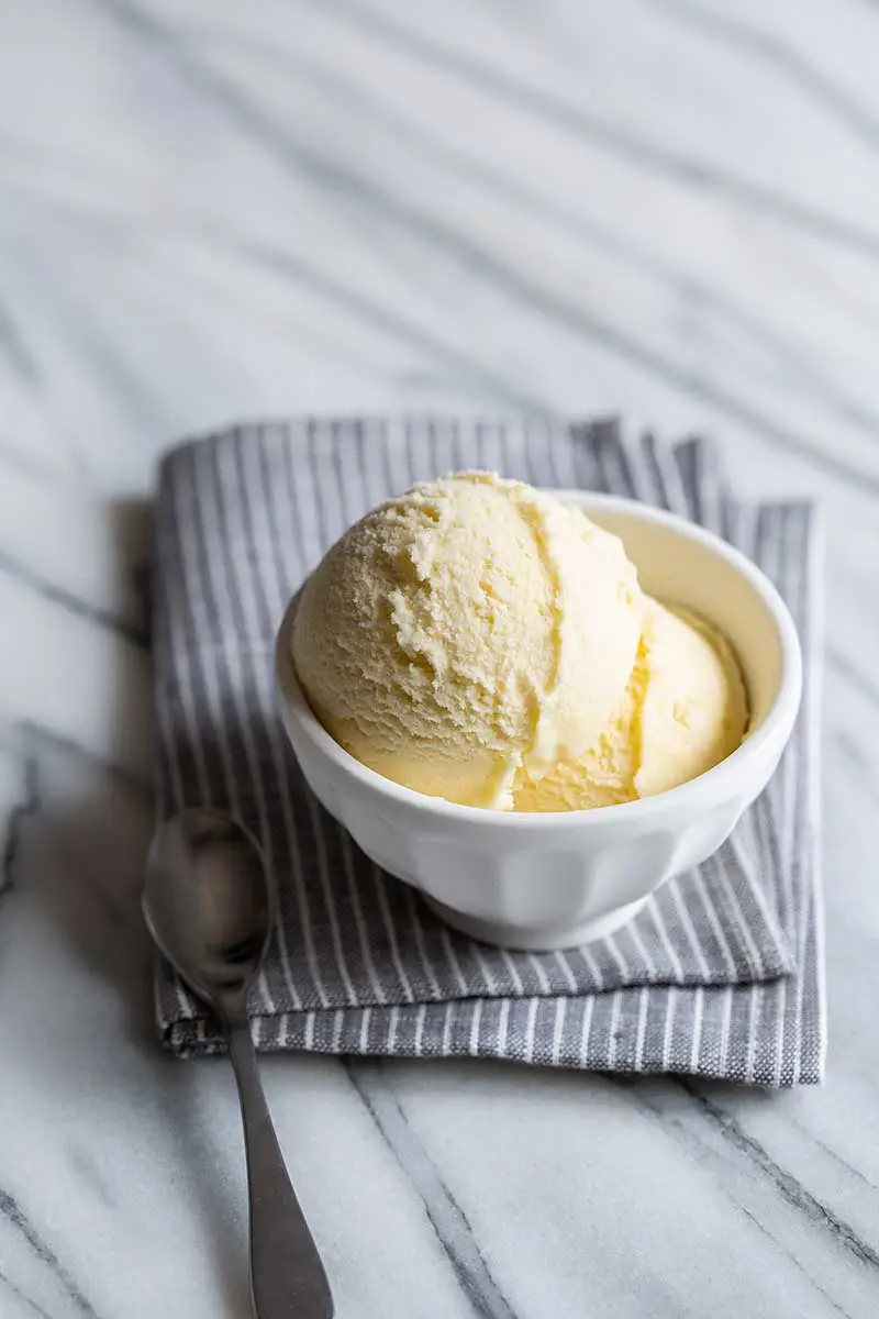 A small bowl of olive oil ice cream on top of a gray striped cloth. 