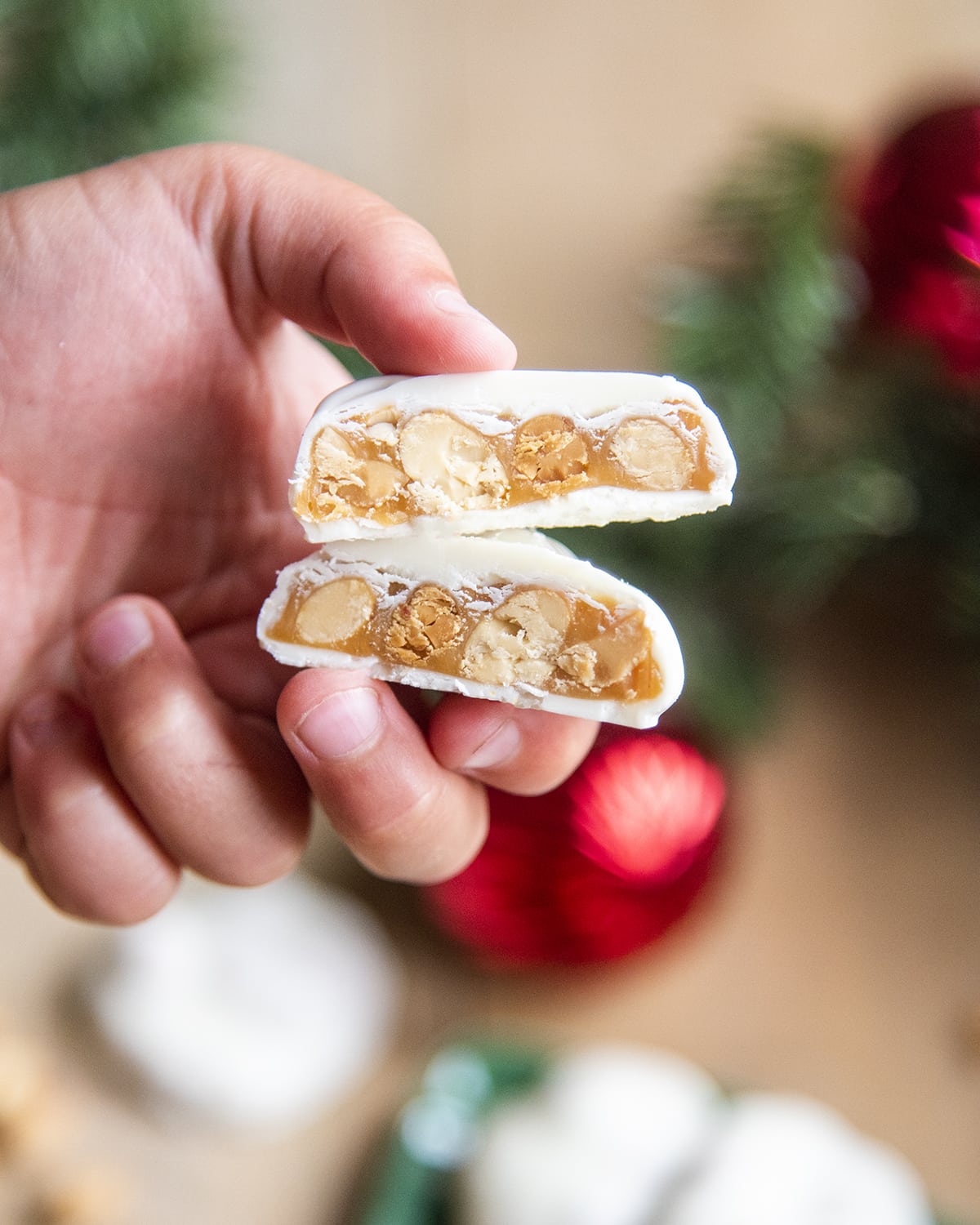 A hand holding two pieces of polar bear paw candies cut in half showing the caramel and pecans in the middle.