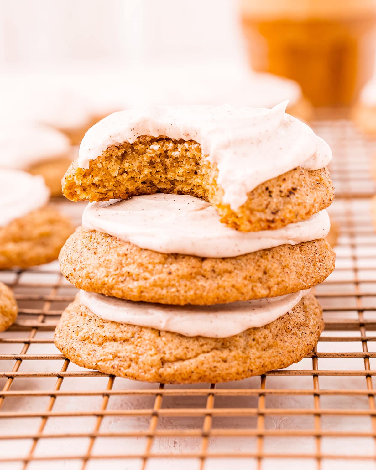 A stack of three pumpkin cookies with spiced cream cheese frosting on top of them. The top cookie has a bite out of it.