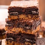 A stack of three slutty brownies with a layer of cookie, Oreo, and brownie on top.