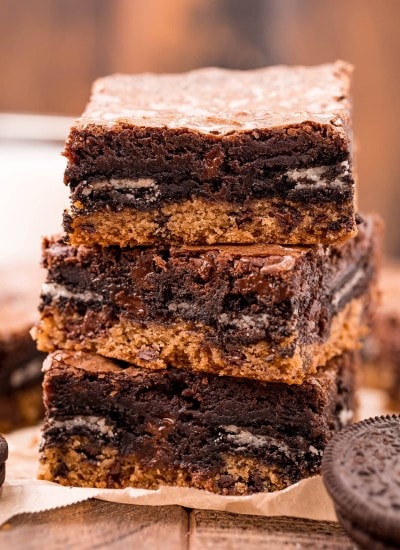 A stack of three slutty brownies with a layer of cookie, Oreo, and brownie on top.