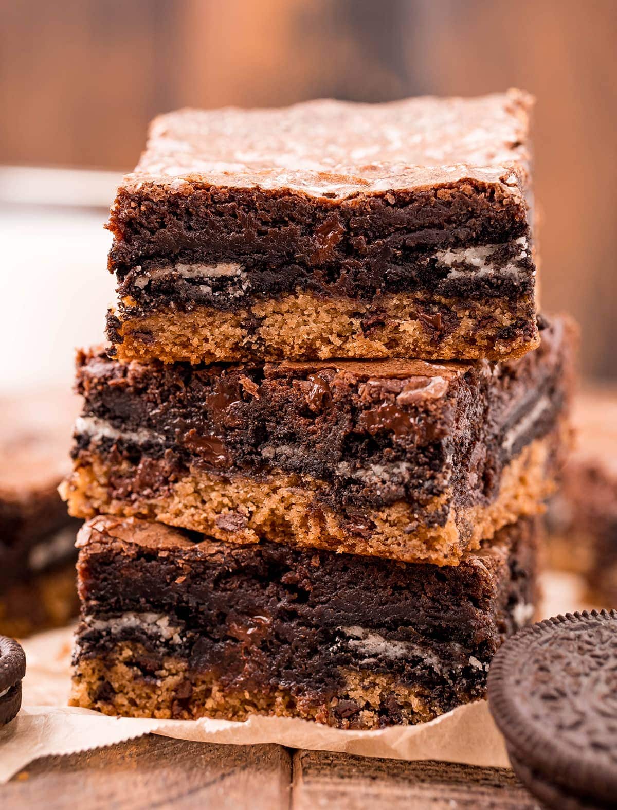 A stack of three slutty brownies with a layer of cookie, Oreo, and brownie on top.