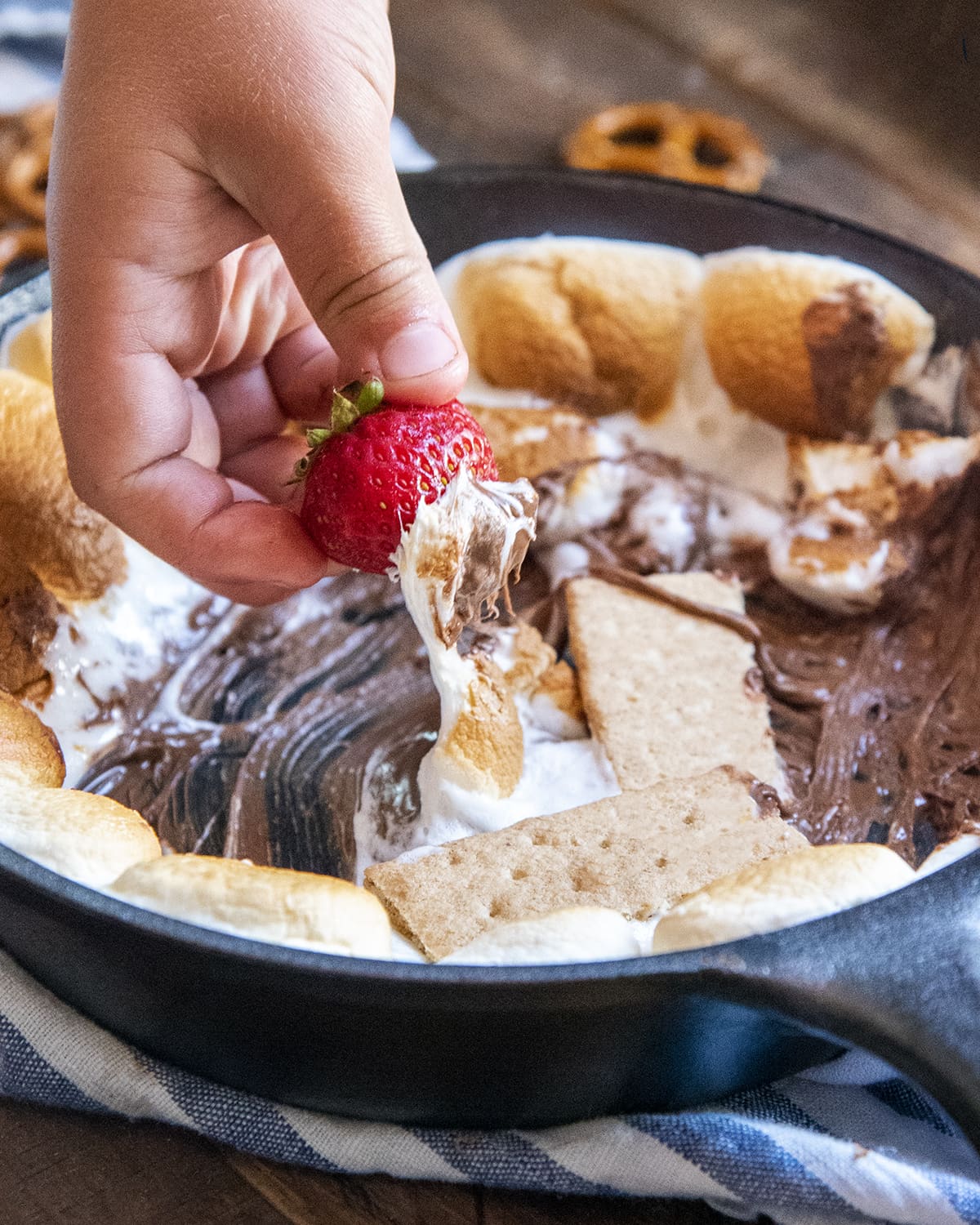 A hand dipping a strawberry into a pan of s'mores dip.