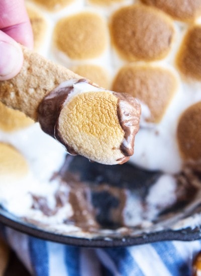 A piece of a graham cracker with chocolate and a toasted marshmallow on it, being held by a hand.