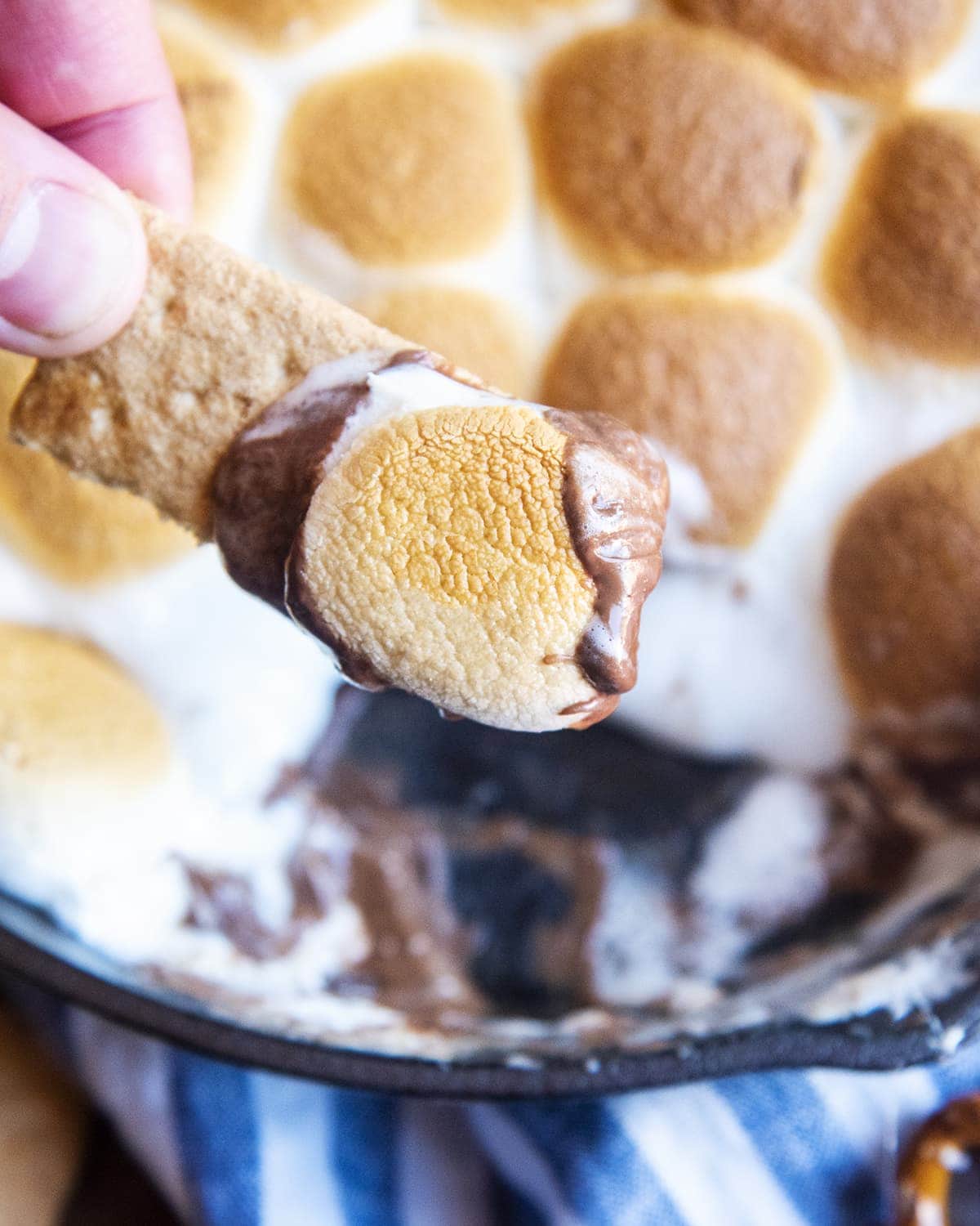 A piece of a graham cracker with chocolate and a toasted marshmallow on it, being held by a hand.