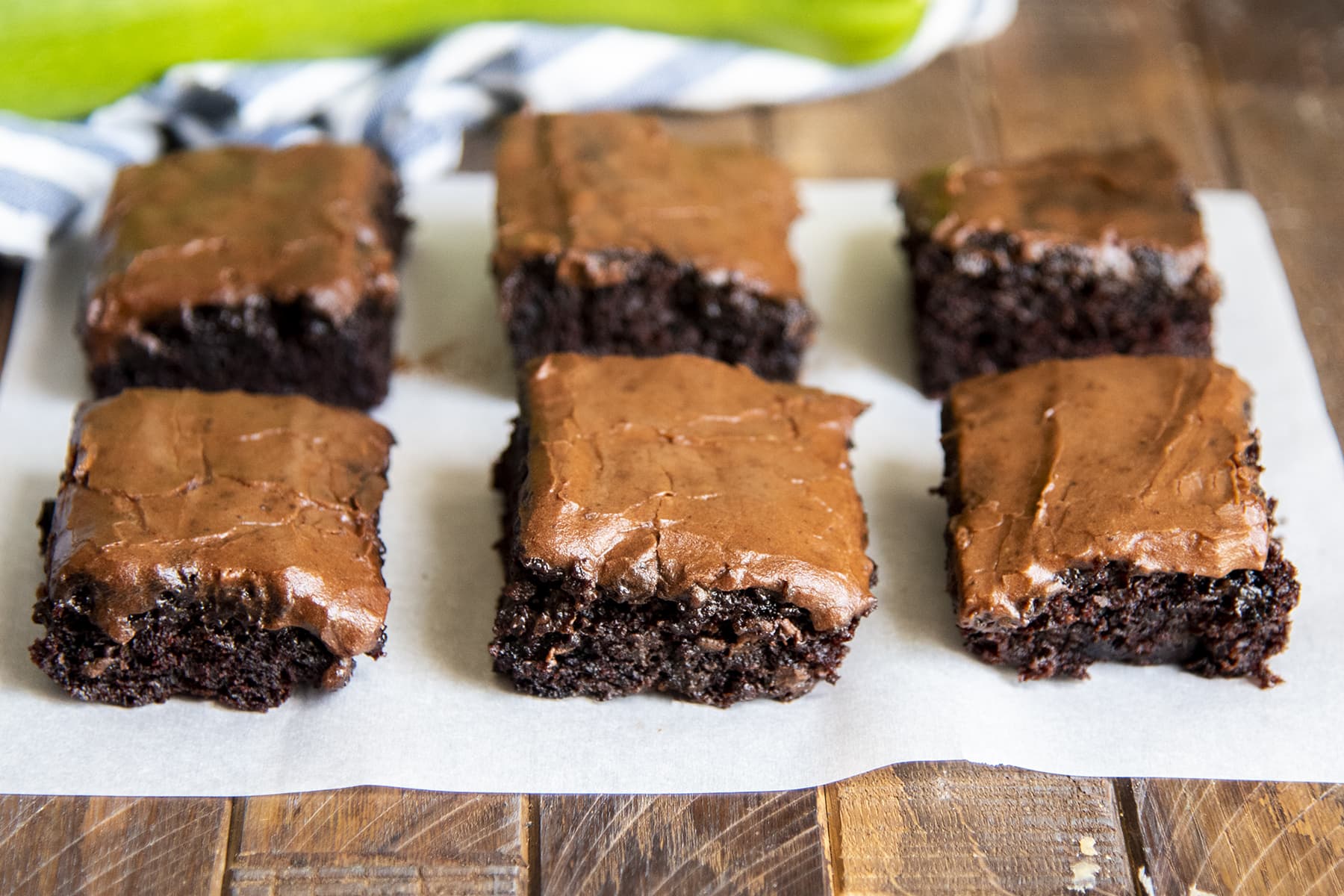 Six frosted brownies on a piece of parchment paper.