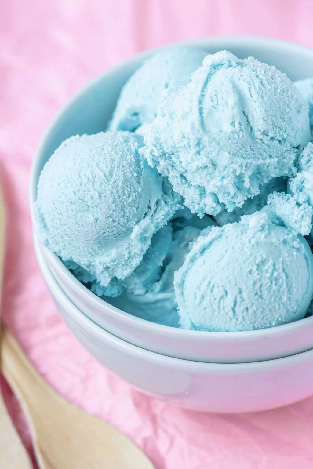 A close up of scoops of blue cotton candy ice cream in a stack of white bowls. 