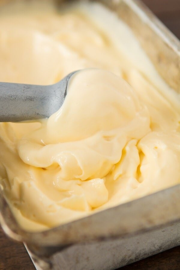 A scoop of lemon ice cream being scooped out of a bread pan of ice cream.