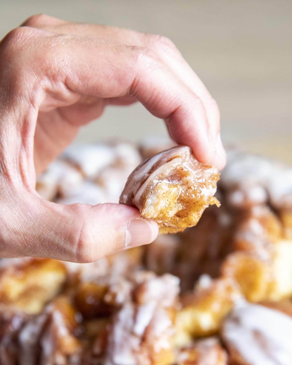 A hand holding a piece of cinnamon roll monkey bread, covered in cinnamon and white icing.