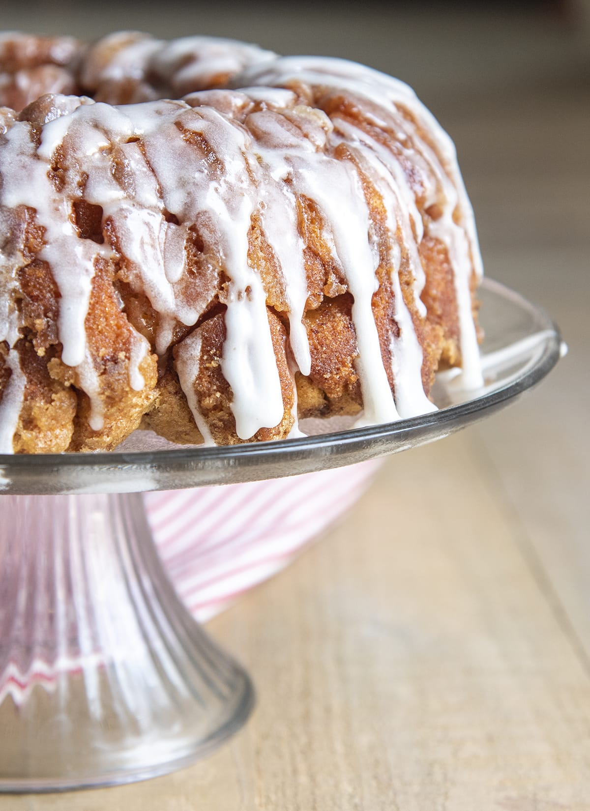 Cinnamon Roll Pull Apart bread on a glass cake stand drizzled in a white icing.