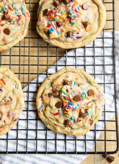 A close up of giant sprinkle and chocolate chip cookies on a cooling rack!