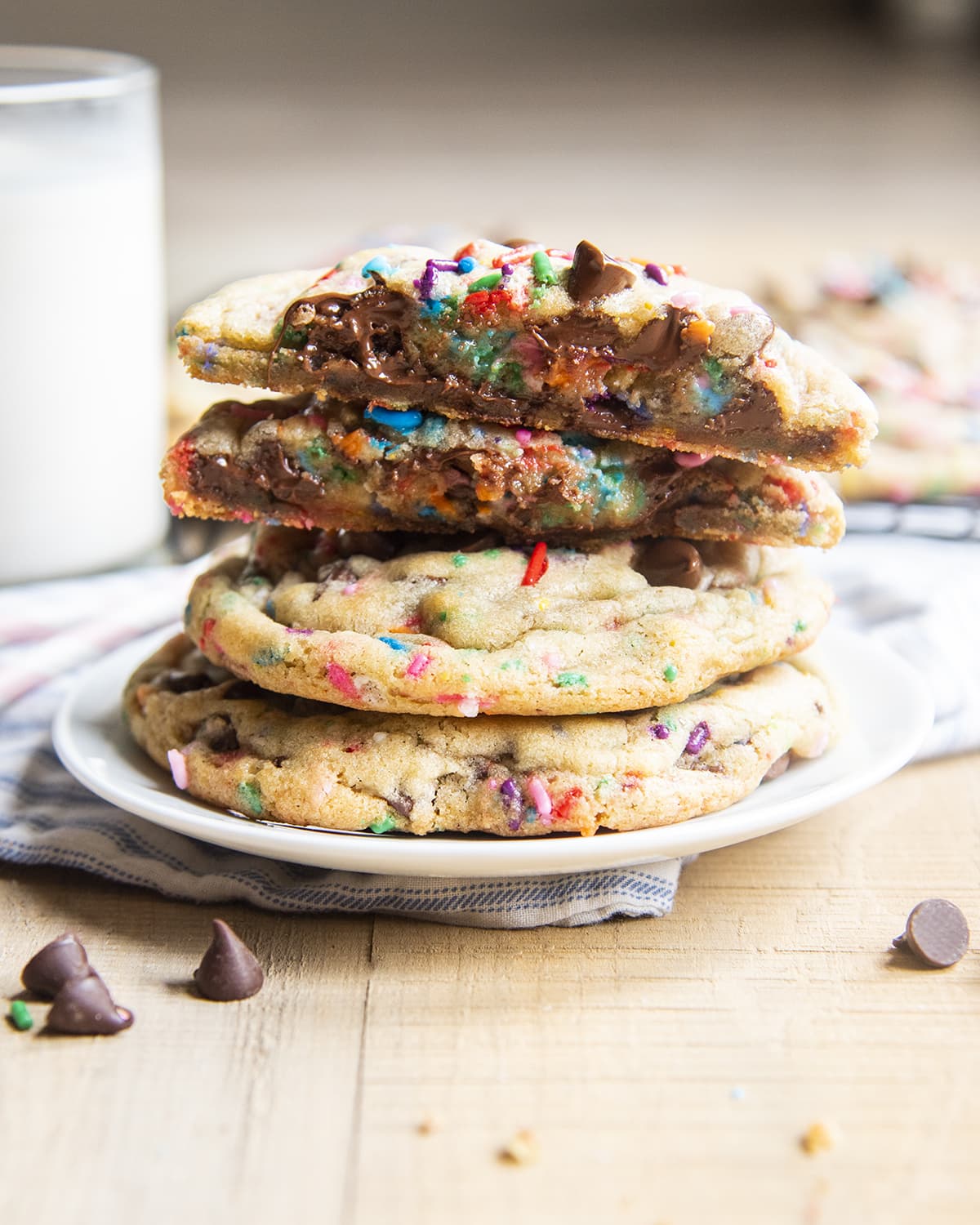 A plate stacked with funfetti chocolate chip cookies. The top is cut in half showing the melty chocolate.