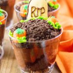A close up of a graveyard pudding cup topped with chocolate cookie crumbs and a cookie "tombstone" saying RIP.