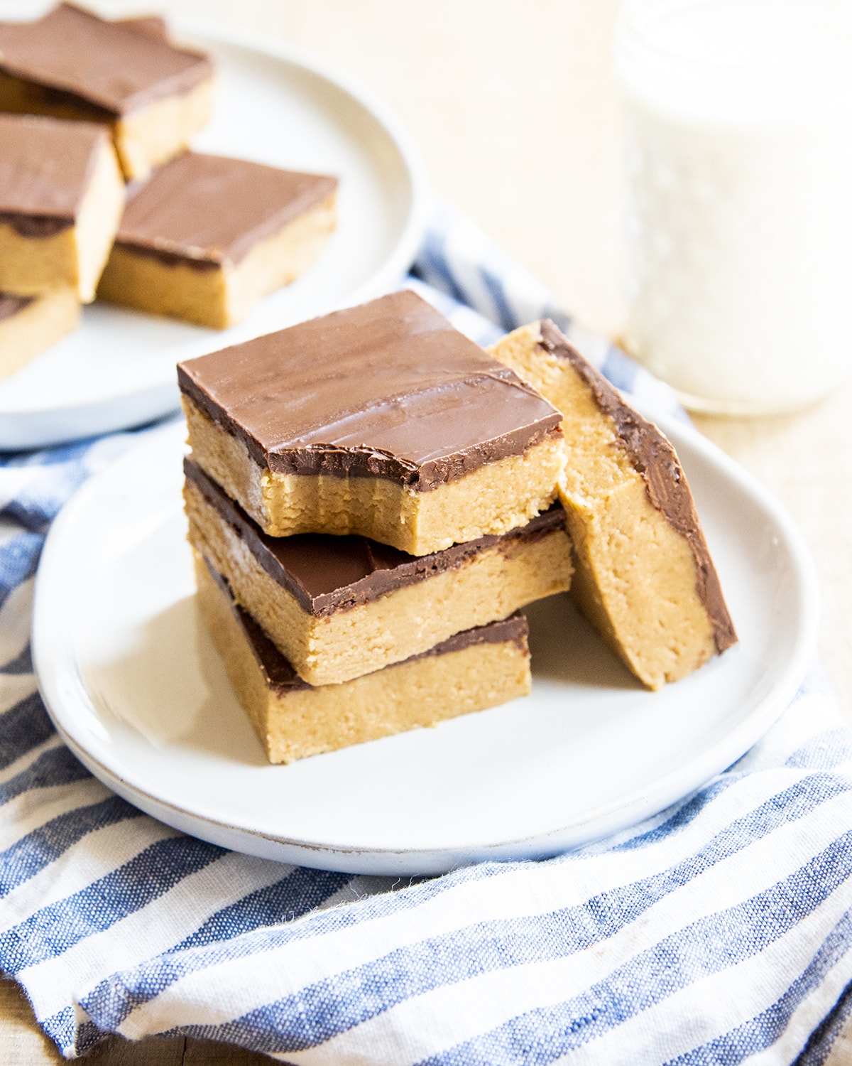 A white plate with a pile of no bake peanut butter bars. The top bar has a bite out of it.