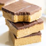 A close up of three no bake chocolate peanut butter bars on a plate, and the top bar has a bite out of it.