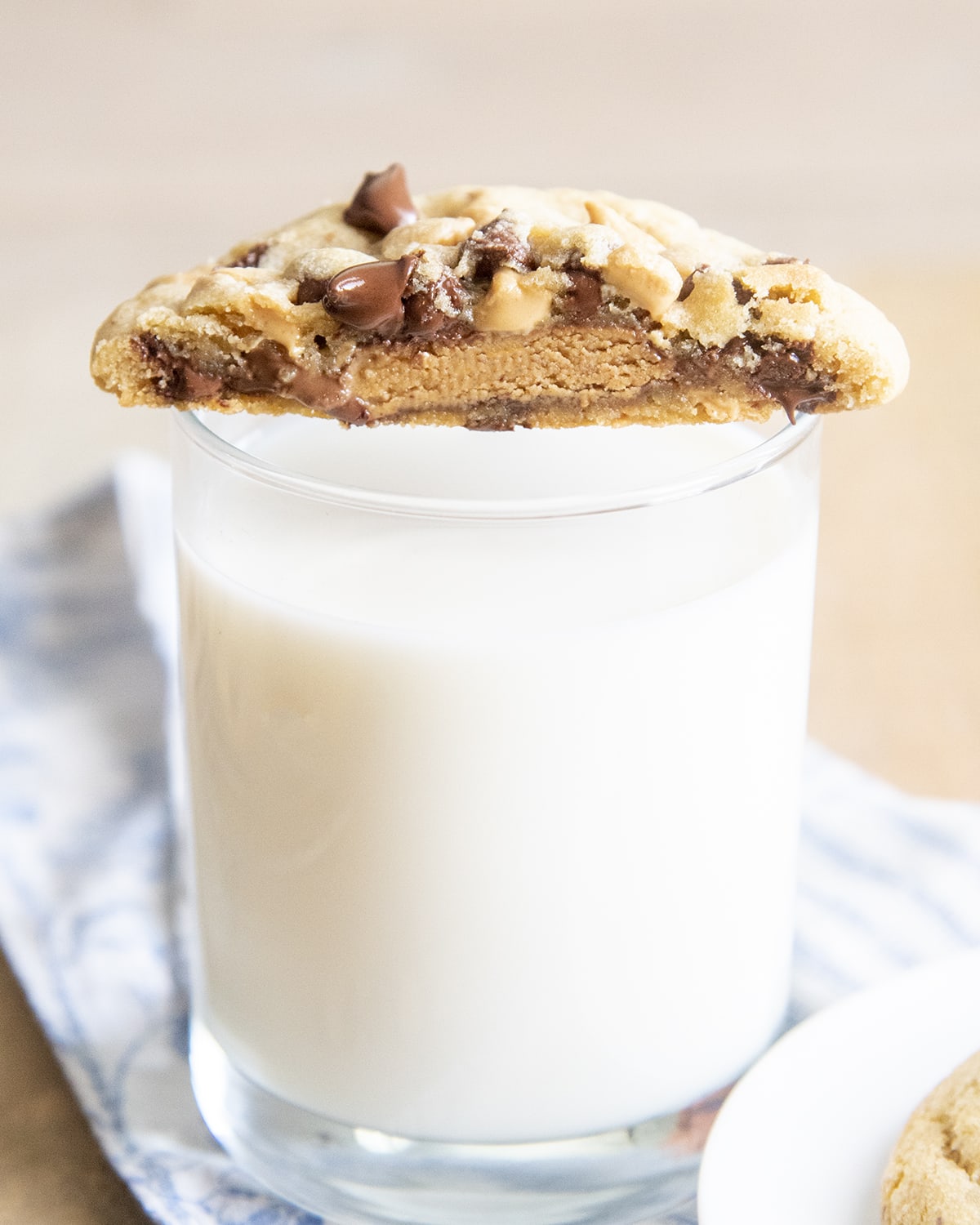 Half a cookie set on a cup of glass, showing the inside of the cookie with a peanut butter cup, and melted chocolate chips.