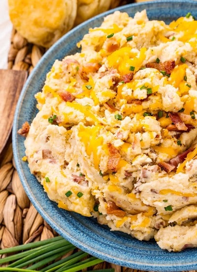 A bowl of loaded mashed potatoes topped with cheese, bacon, and chives.