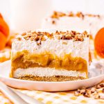A piece of a layered dessert with graham cracker crust, no bake cheesecake, pumpkin pudding, and whipped cream.