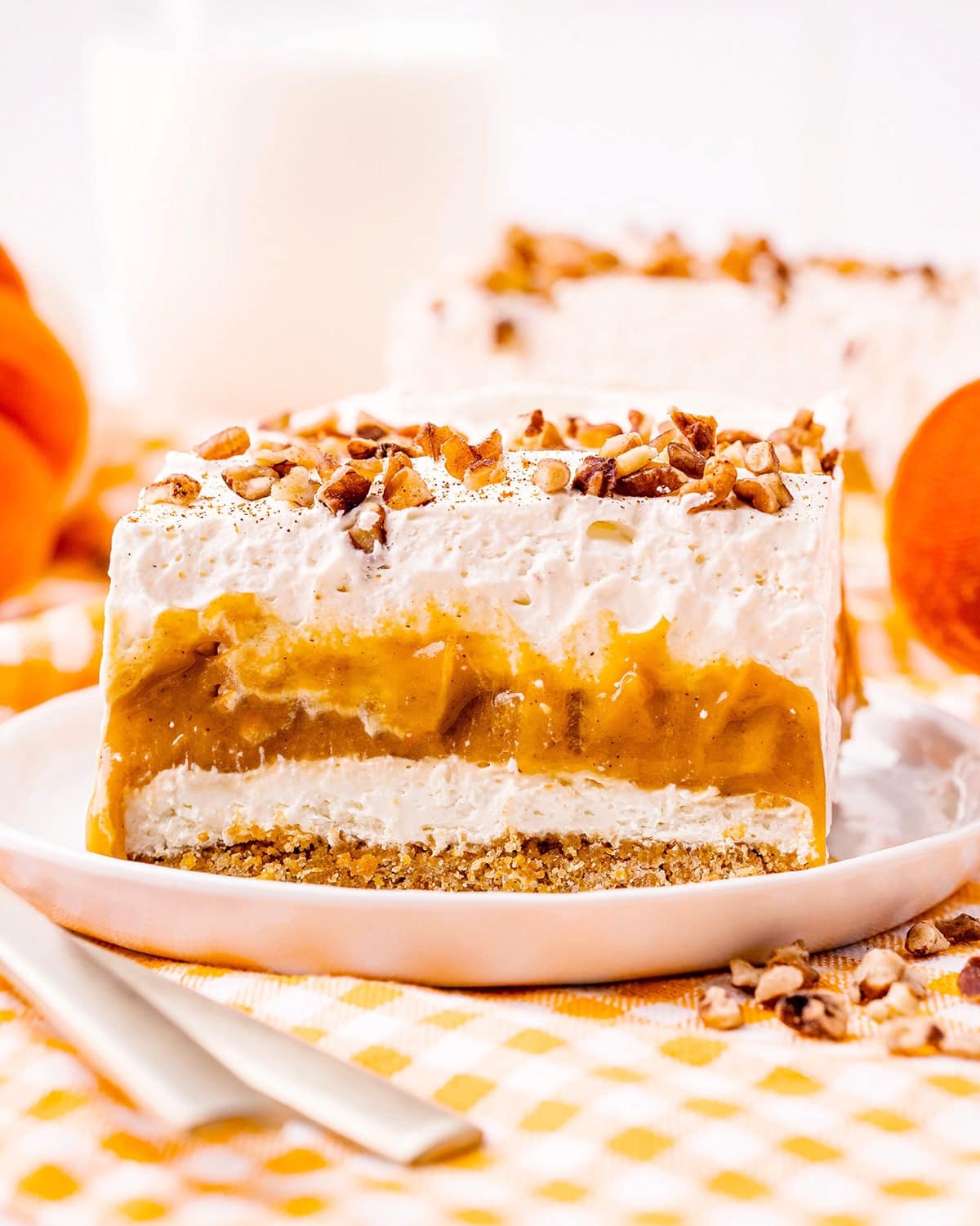 A piece of a layered dessert with graham cracker crust, no bake cheesecake, pumpkin pudding, and whipped cream.