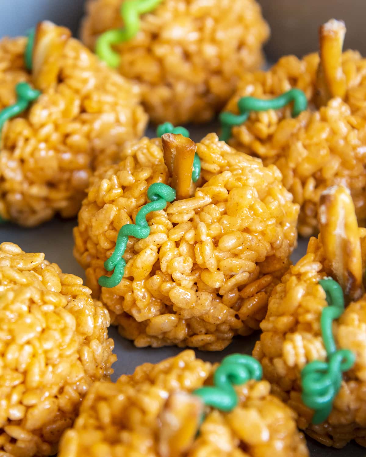 Pumpkin Rice Krispie Treats close to one another in a pan. They have green candy "vines" and pretzel "stems".
