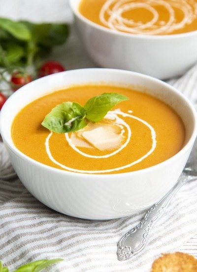 A bowl of roasted tomato soup topped with swirls of heavy cream, and fresh basil leaves.