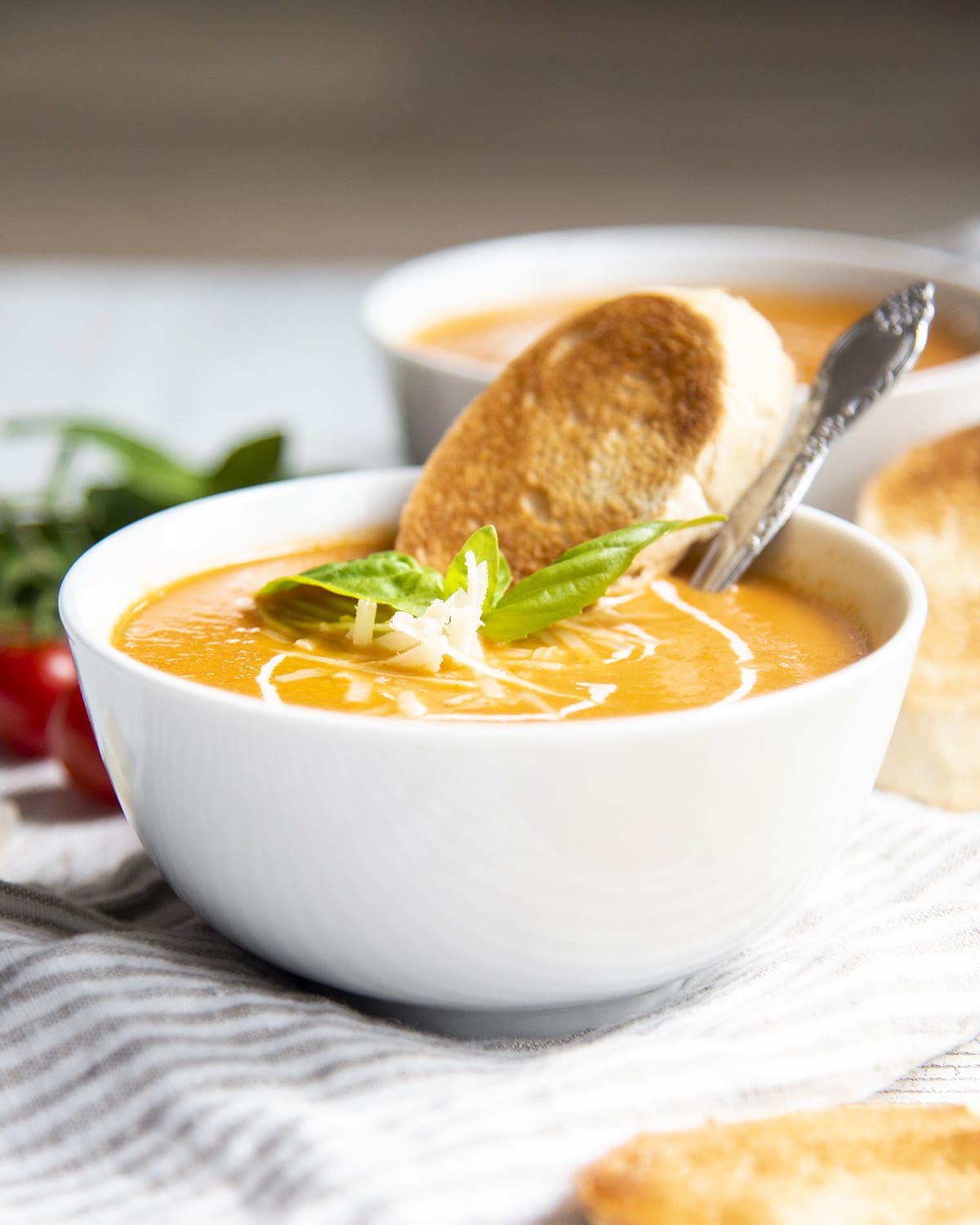 A bowl of roasted tomato soup with a piece of toasted bread in it.