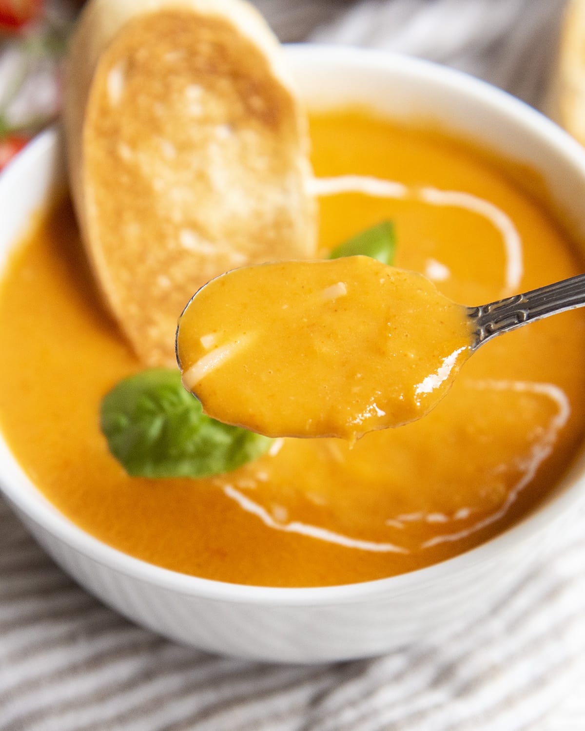 A spoonful of tomato soup above a bowl.