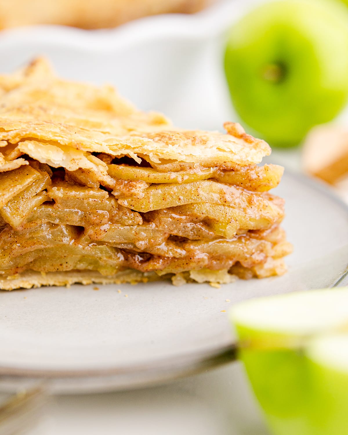 A close up of a slice of apple pie showing all the layers of apple slices and the crust on top.
